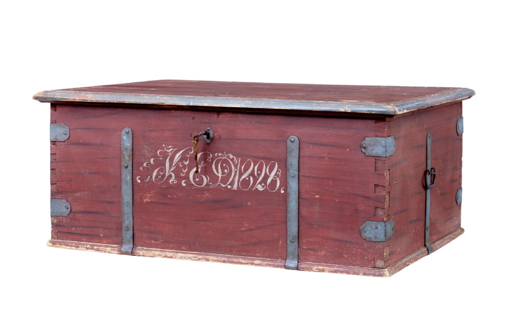 A 19th-century red-painted pine blanket box featuring white hand-painted script dated 1828 and wrought iron corner brackets.
