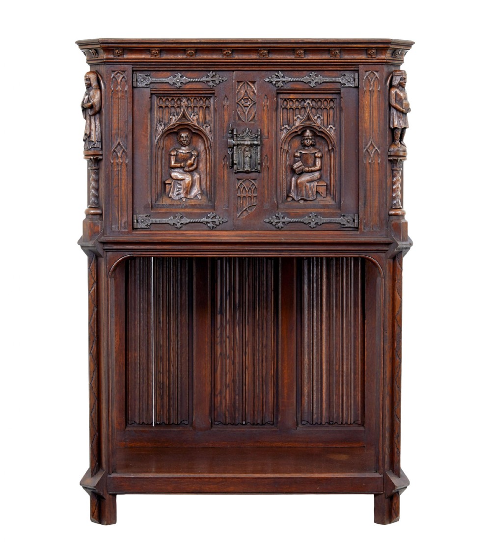 A dark oak Renaissance Revival cupboard featuring carved human figures, gothic arched panels, iron hardware, and an open lower shelf. View II