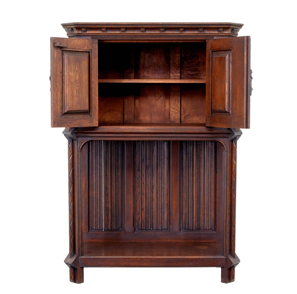 A dark oak Renaissance Revival cupboard featuring carved human figures, gothic arched panels, iron hardware, and an open lower shelf. View III