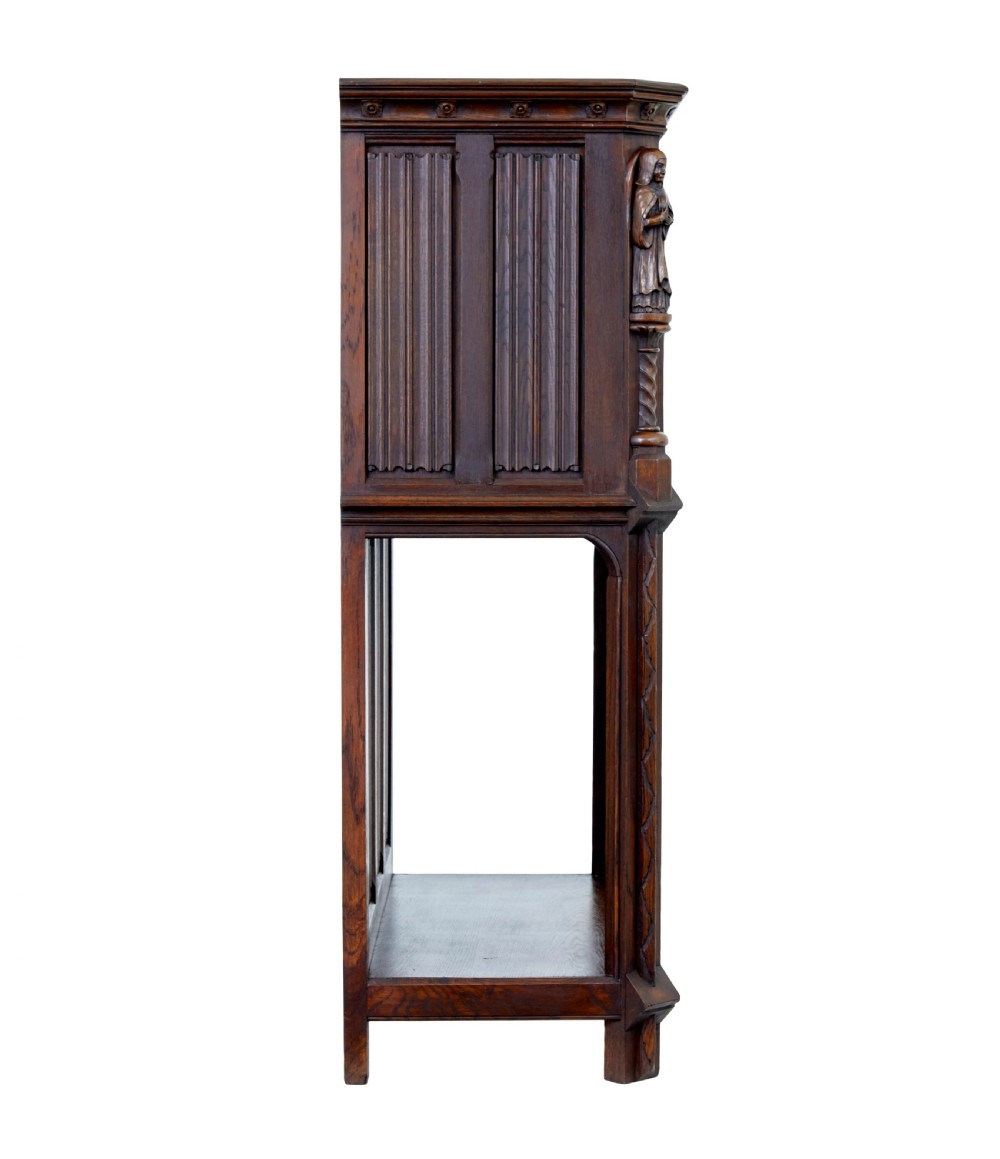 A dark oak Renaissance Revival cupboard featuring carved human figures, gothic arched panels, iron hardware, and an open lower shelf. View VI