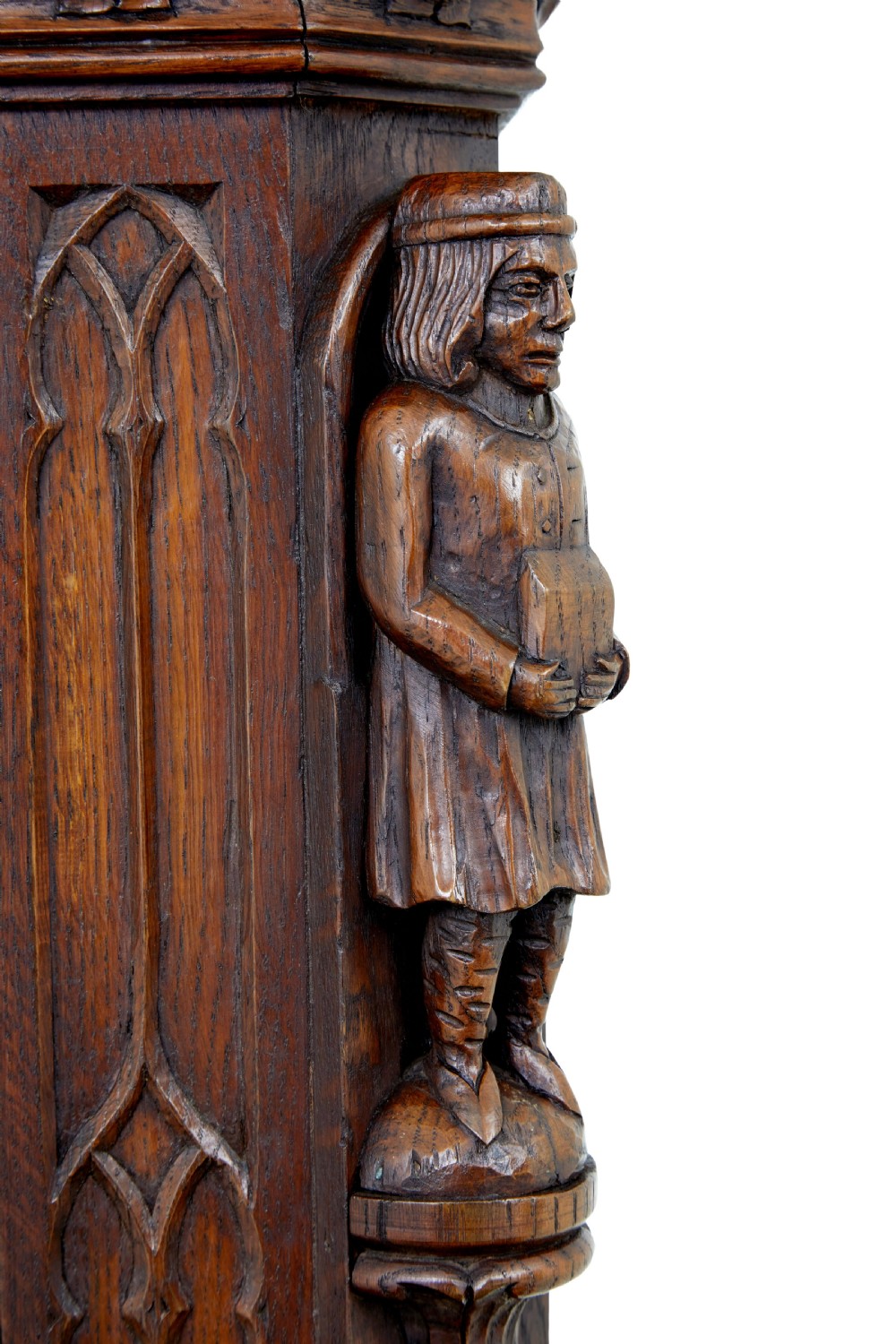 A dark oak Renaissance Revival cupboard featuring carved human figures, gothic arched panels, iron hardware, and an open lower shelf. View VIII