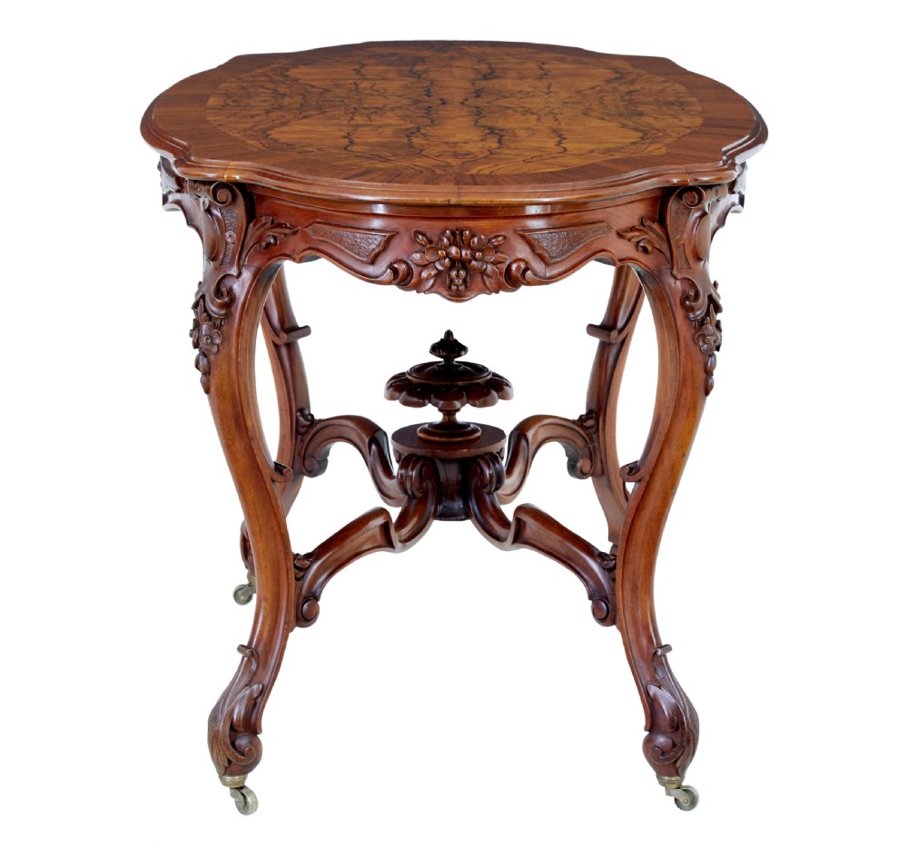 A 19th-century carved walnut occasional table featuring a shaped burr walnut top, ornate floral apron, cabriole legs, and a carved central stretcher finial on castors. View II