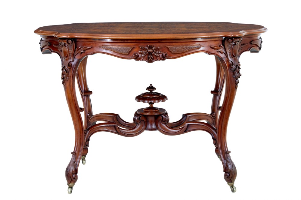 A 19th-century carved walnut occasional table featuring a shaped burr walnut top, ornate floral apron, cabriole legs, and a carved central stretcher finial on castors. View III