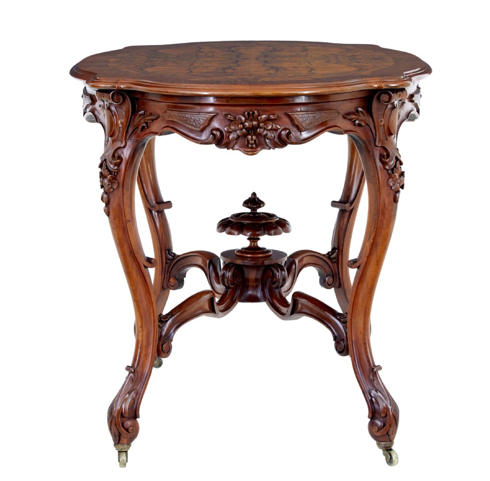 A 19th-century carved walnut occasional table featuring a shaped burr walnut top, ornate floral apron, cabriole legs, and a carved central stretcher finial on castors. View IV
