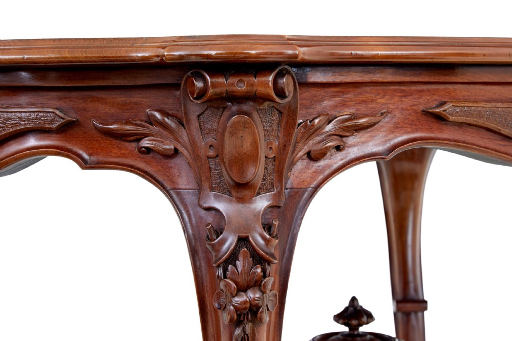 A 19th-century carved walnut occasional table featuring a shaped burr walnut top, ornate floral apron, cabriole legs, and a carved central stretcher finial on castors. View VI