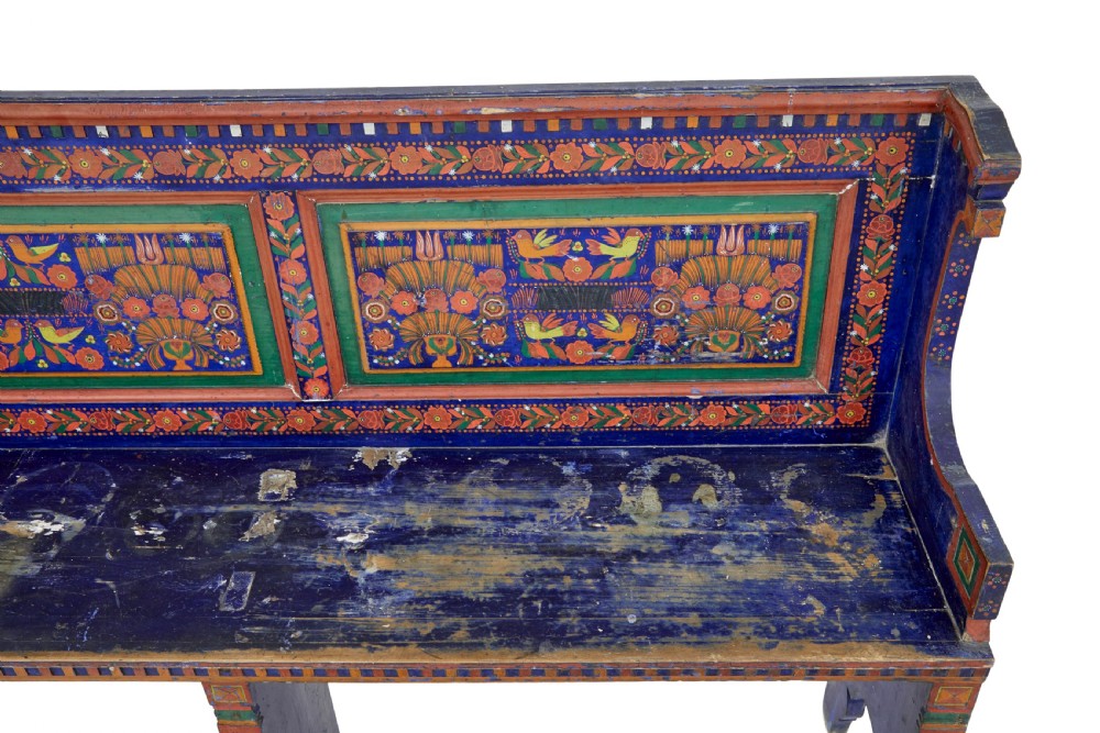 A nineteenth-century L-shaped wooden corner bench featuring hand-painted floral panels in red, green, and orange over a deep blue frame. View X