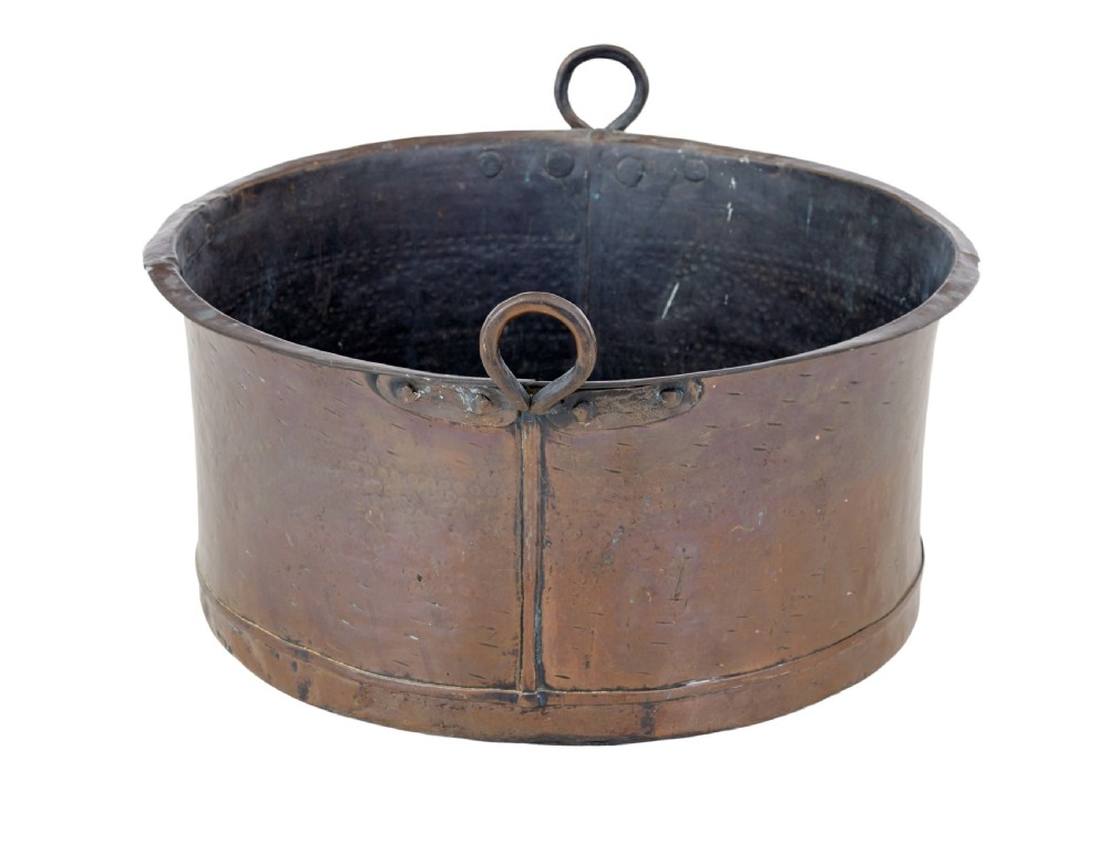 A large, circular nineteenth-century copper vessel with deep sides, hand-riveted seams, and two upright loop handles.