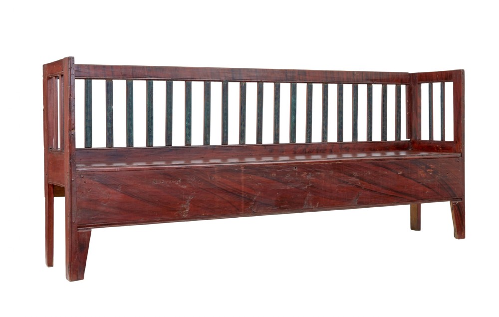 A mid 19th-century Swedish rustic pine bench featuring a dark red painted finish, a spindle backrest with contrasting dark green slats, and an enclosed box base.