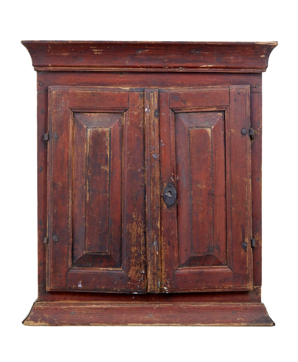 An early 19th-century Swedish painted pine wall cupboard featuring double panelled doors in a terracotta finish with moulded borders and central iron lock plate.