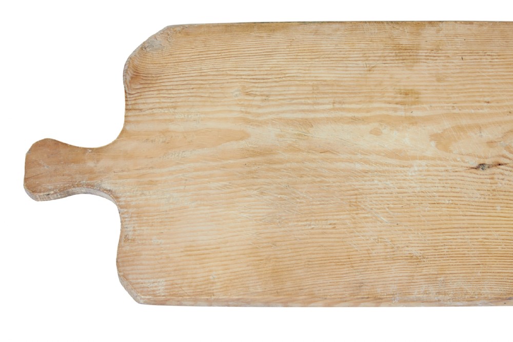 A long rectangular pale pine breadboard featuring a shaped handle at one end and natural timber grain with a knot. View IV