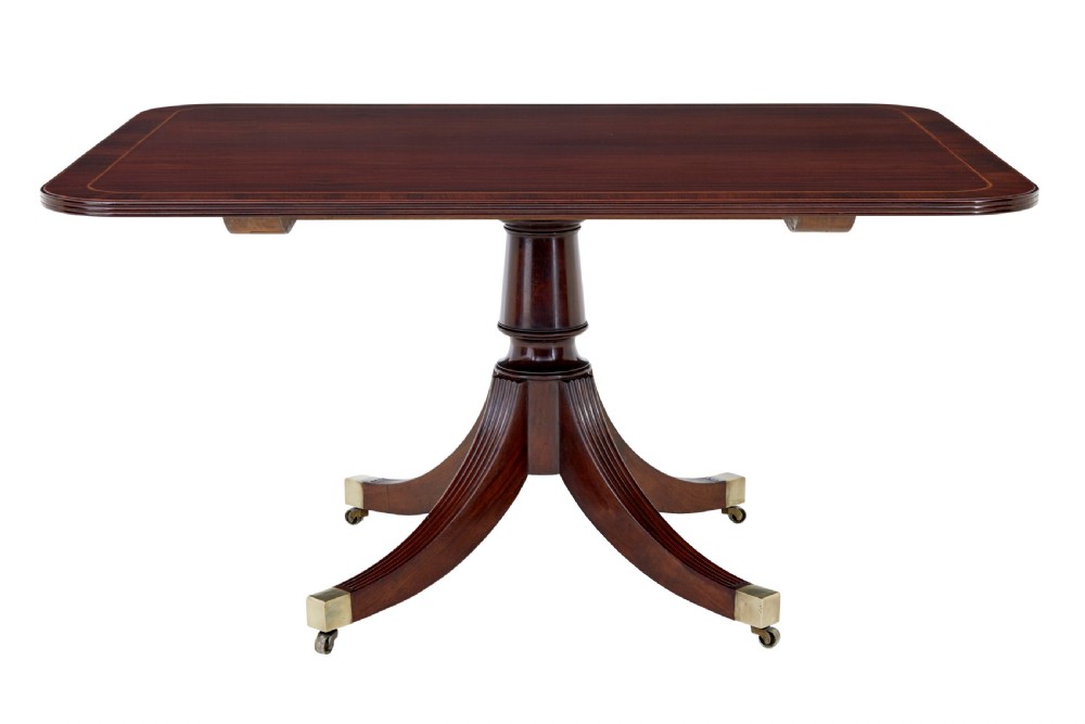 An early 19th-century Regency mahogany breakfast table featuring an inlaid rectangular top with rounded corners, supported by a turned pedestal and four reeded legs with brass castors.