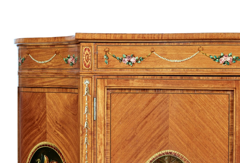 A late 19th-century Sheraton Revival satinwood cabinet featuring hand-painted floral swags, classical figurative oval panels, intricate wood marquetry, and tapered legs. View X