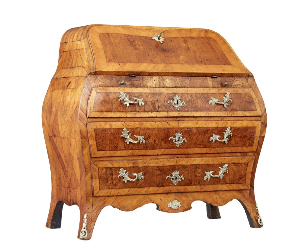An 18th-century Rococo bureau crafted from yew and elm wood featuring a curved bombe body, slant-front writing slope, three drawers, and decorative cast brass handles.