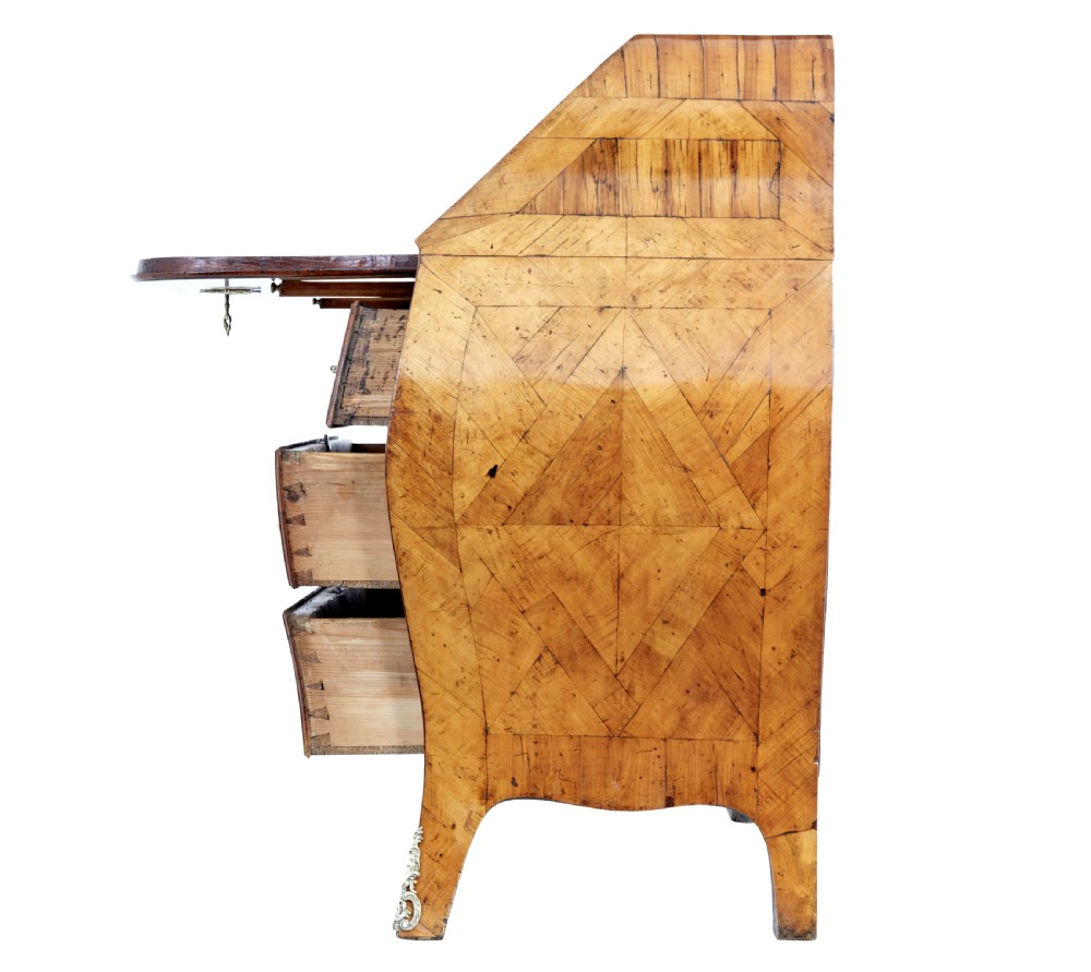 An 18th-century Rococo bureau crafted from yew and elm wood featuring a curved bombe body, slant-front writing slope, three drawers, and decorative cast brass handles. View V