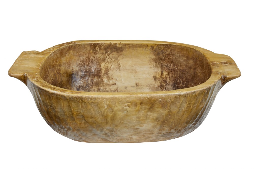 A large hand-carved wooden bowl with integrated side handles and visible adze tool marks across the light brown timber surface.