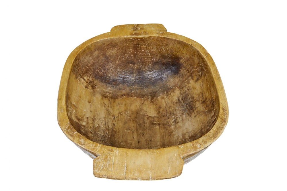 A large hand-carved wooden bowl with integrated side handles and visible adze tool marks across the light brown timber surface. View II