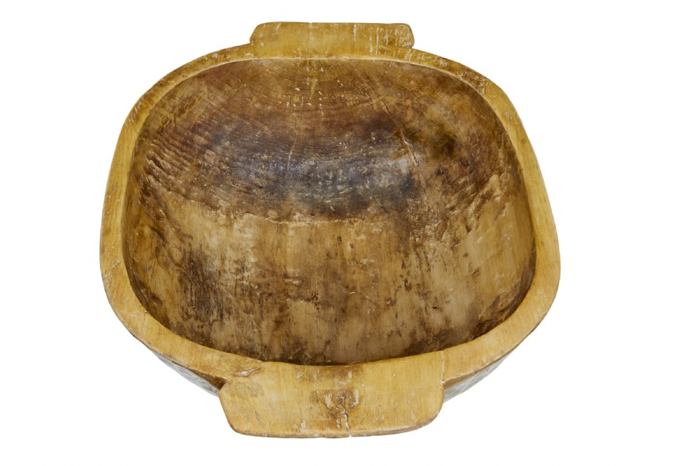 A large hand-carved wooden bowl with integrated side handles and visible adze tool marks across the light brown timber surface. View III