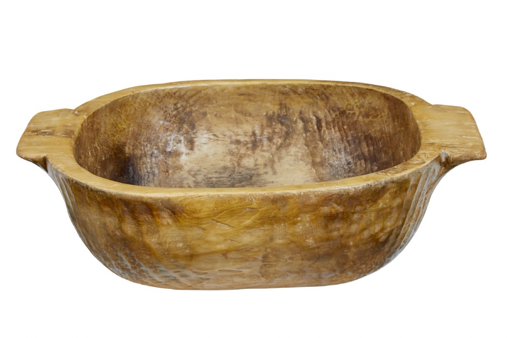 A large hand-carved wooden bowl with integrated side handles and visible adze tool marks across the light brown timber surface. View IV