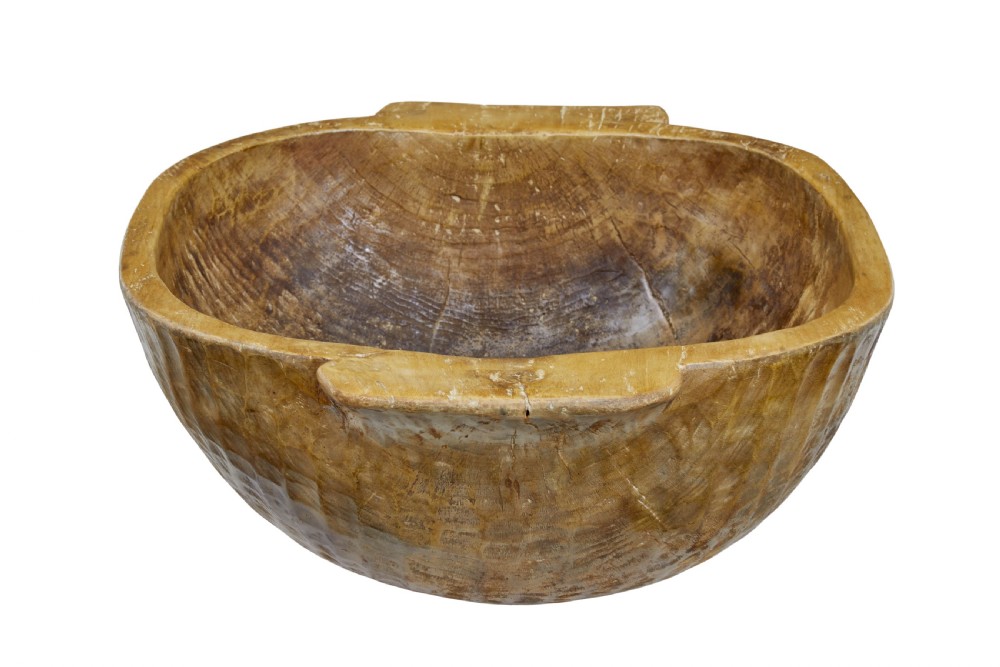 A large hand-carved wooden bowl with integrated side handles and visible adze tool marks across the light brown timber surface. View V