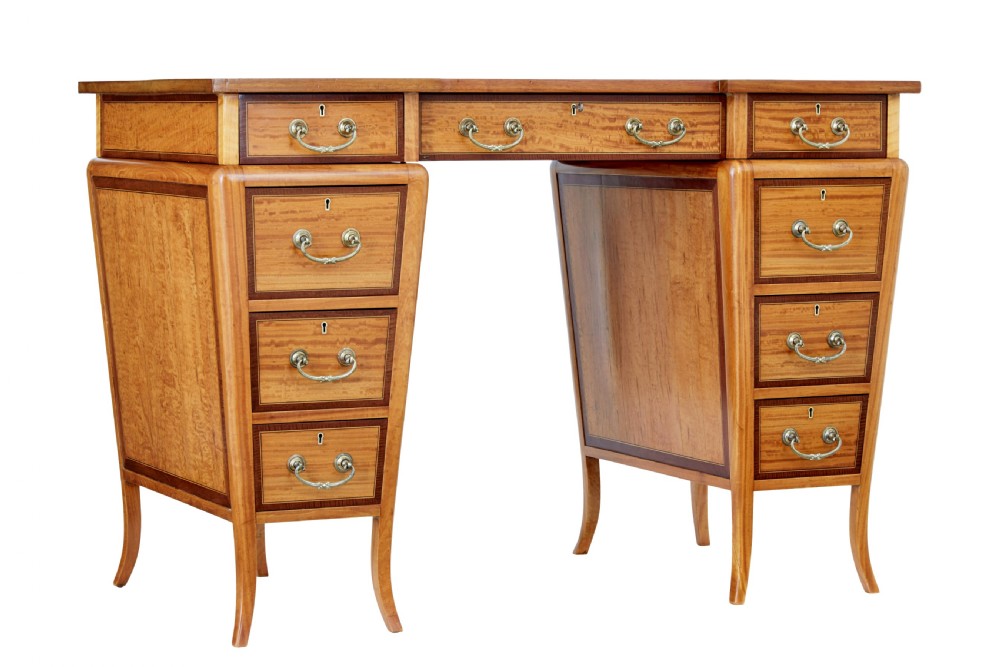 An early 20th-century Sheraton Revival satinwood pedestal desk featuring inlaid mahogany crossbanding, seven drawers with brass handles, and gently splayed legs.