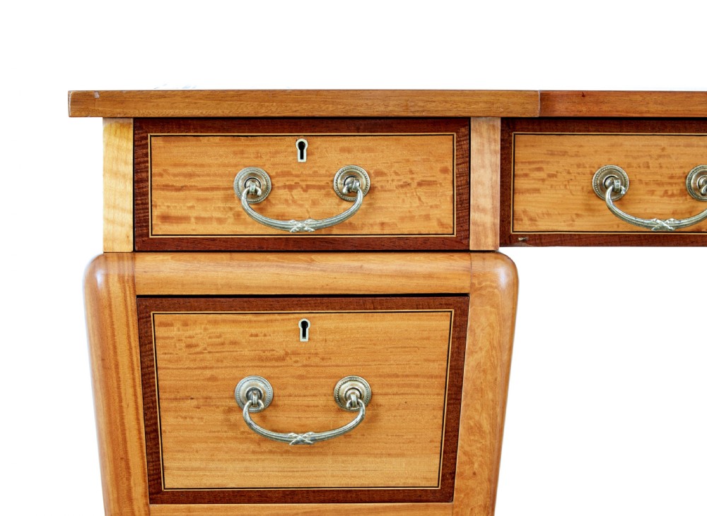 An early 20th-century Sheraton Revival satinwood pedestal desk featuring inlaid mahogany crossbanding, seven drawers with brass handles, and gently splayed legs. View VIII