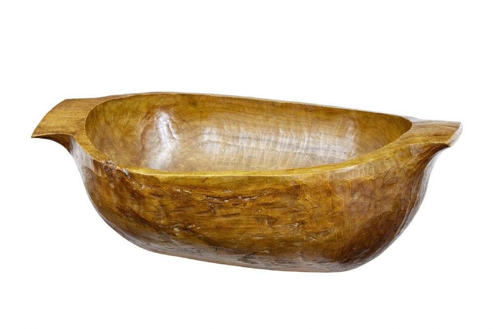 A large hand-carved wooden dough bowl with integrated end handles and a polished warm brown finish displaying visible adze marks.