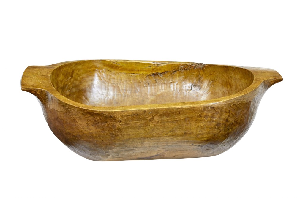 A large hand-carved wooden dough bowl with integrated end handles and a polished warm brown finish displaying visible adze marks. View V