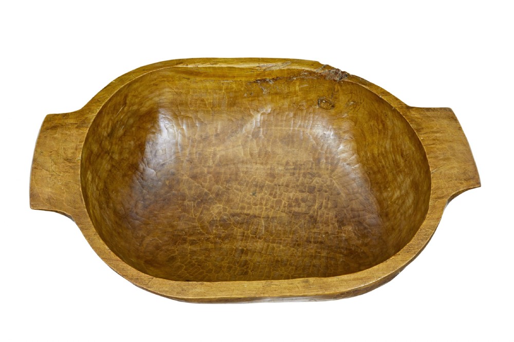 A large hand-carved wooden dough bowl with integrated end handles and a polished warm brown finish displaying visible adze marks. View VI