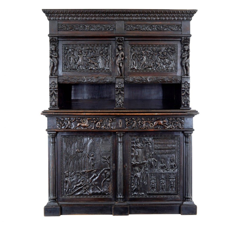 A large 19th-century Flemish dark carved oak cabinet featuring intricate relief panels depicting human figures and architectural details.