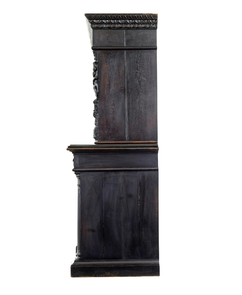 A large 19th-century Flemish dark carved oak cabinet featuring intricate relief panels depicting human figures and architectural details. View V