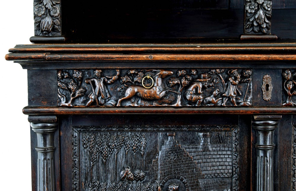 A large 19th-century Flemish dark carved oak cabinet featuring intricate relief panels depicting human figures and architectural details. View VI