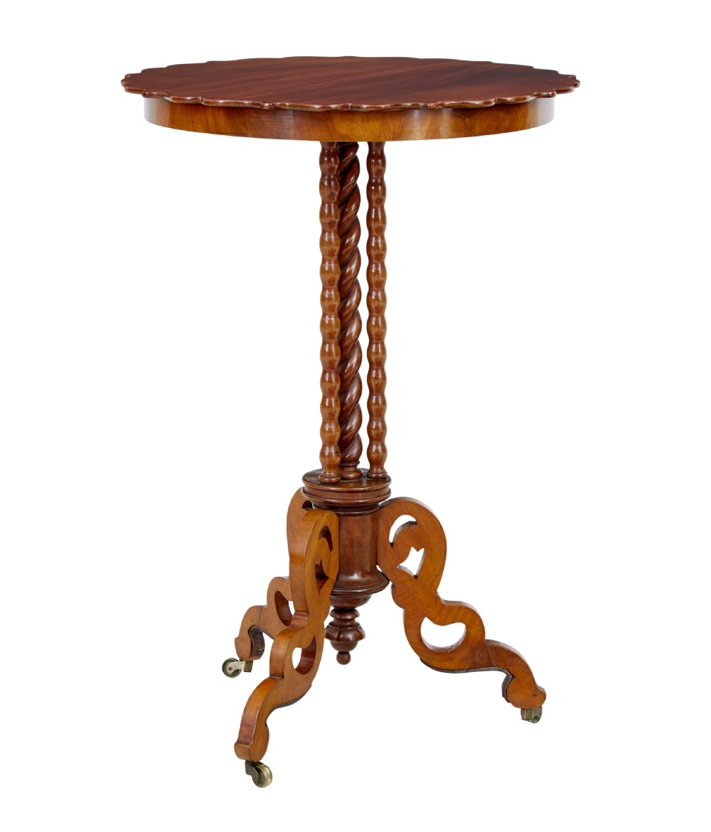 A late 19th-century mahogany occasional table featuring a scalloped piecrust top, central bobbin-turned supports, and a tripod scroll base with brass castors.