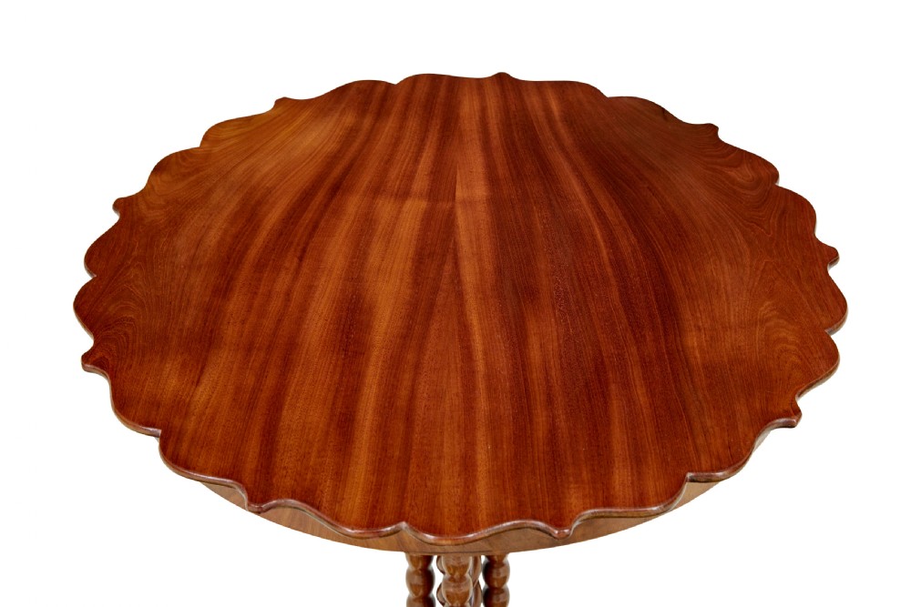 A late 19th-century mahogany occasional table featuring a scalloped piecrust top, central bobbin-turned supports, and a tripod scroll base with brass castors. View IV