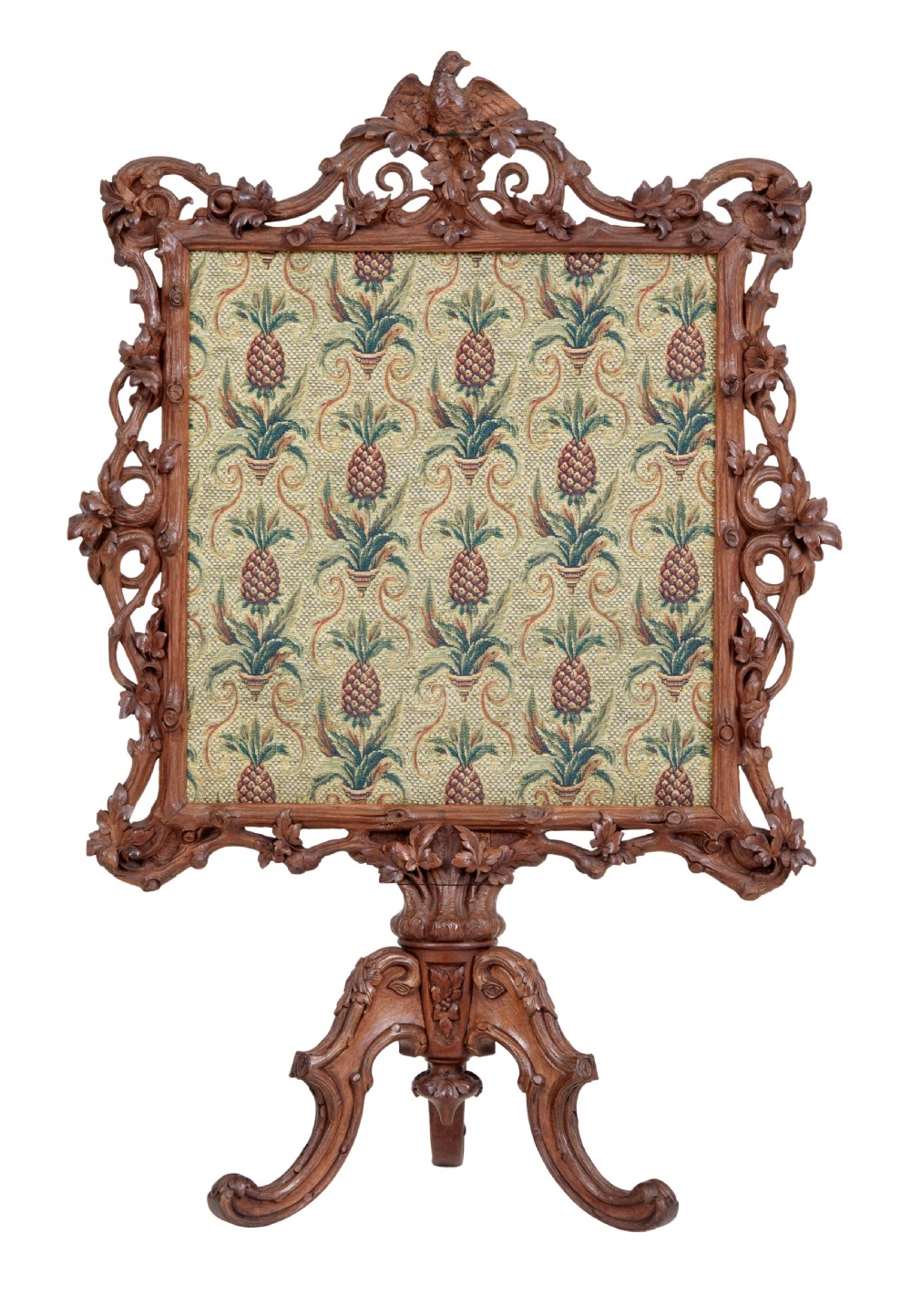A carved oak tripod fire screen with a crest carved as a bird surrounding a woven tapestry panel featuring pineapple motifs.
