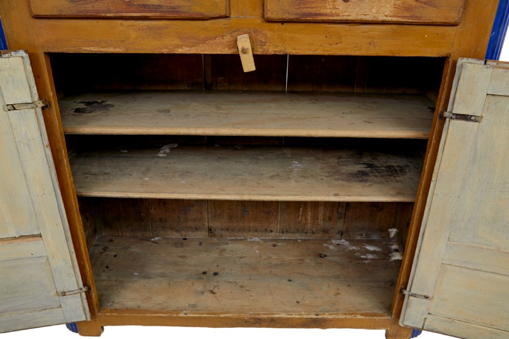 A 19th-century Swedish pine kitchen cupboard with ochre faux-grained body, vibrant blue fluted columns, two top drawers, and blue panelled double doors. View IX