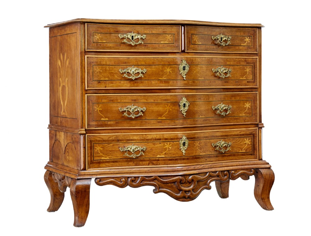 An early nineteenth-century Swedish oak chest of drawers featuring detailed botanical wood inlay, a carved apron, and decorative brass hardware.