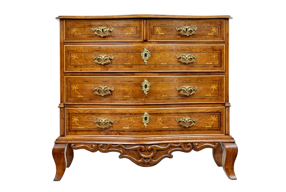 An early nineteenth-century Swedish oak chest of drawers featuring detailed botanical wood inlay, a carved apron, and decorative brass hardware. View II