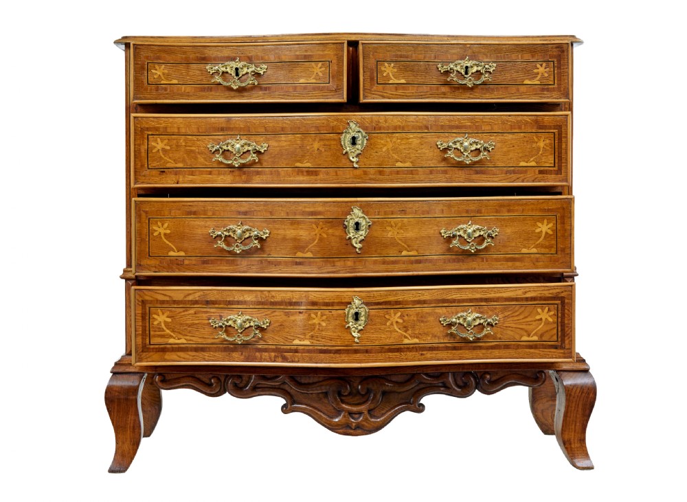 An early nineteenth-century Swedish oak chest of drawers featuring detailed botanical wood inlay, a carved apron, and decorative brass hardware. View III