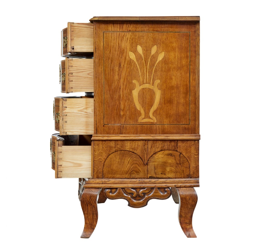 An early nineteenth-century Swedish oak chest of drawers featuring detailed botanical wood inlay, a carved apron, and decorative brass hardware. View V