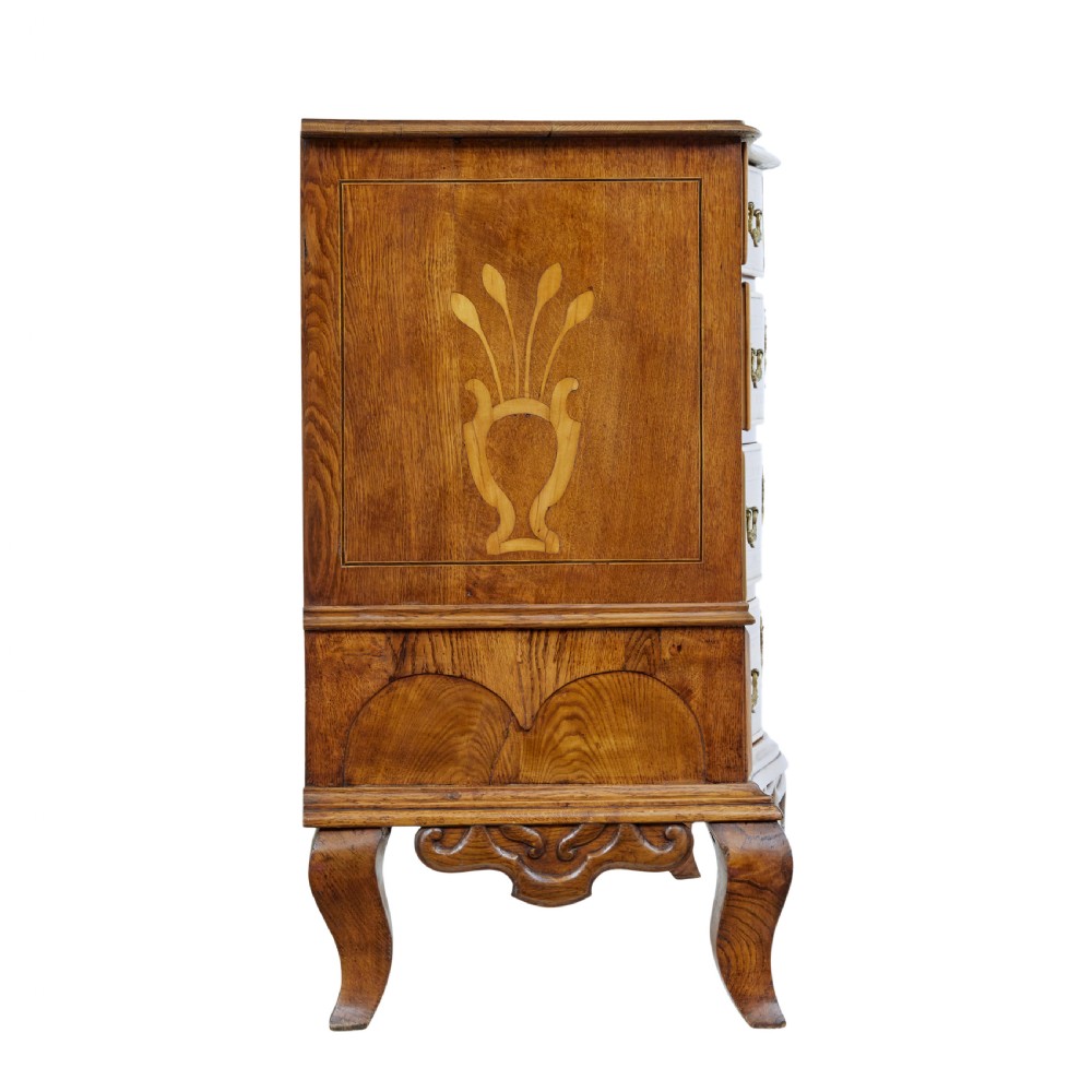 An early nineteenth-century Swedish oak chest of drawers featuring detailed botanical wood inlay, a carved apron, and decorative brass hardware. View VII