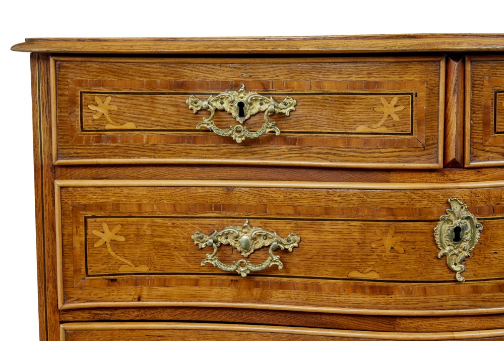 An early nineteenth-century Swedish oak chest of drawers featuring detailed botanical wood inlay, a carved apron, and decorative brass hardware. View IX