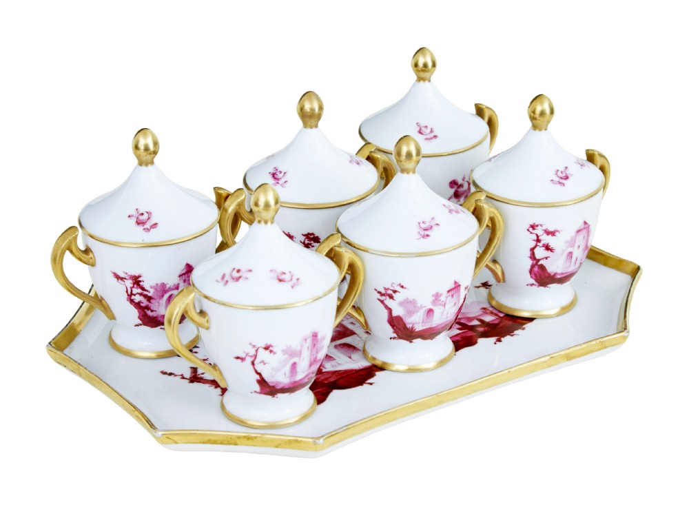 A seven-piece French porcelain dessert set featuring six twin-handled covered cream pots and a matching shaped tray, decorated with pink landscape scenes and gilded handles. View II