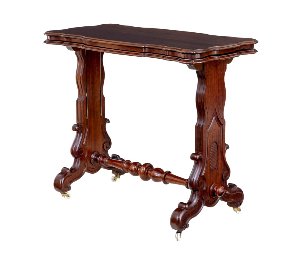 A 19th-century Victorian walnut metamorphic dumb waiter featuring a serpentine moulded top, carved C-scroll side supports, a turned stretcher, and brass castors.