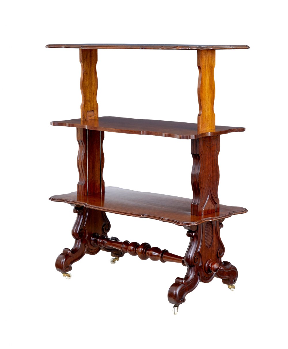 A 19th-century Victorian walnut metamorphic dumb waiter featuring a serpentine moulded top, carved C-scroll side supports, a turned stretcher, and brass castors. View II