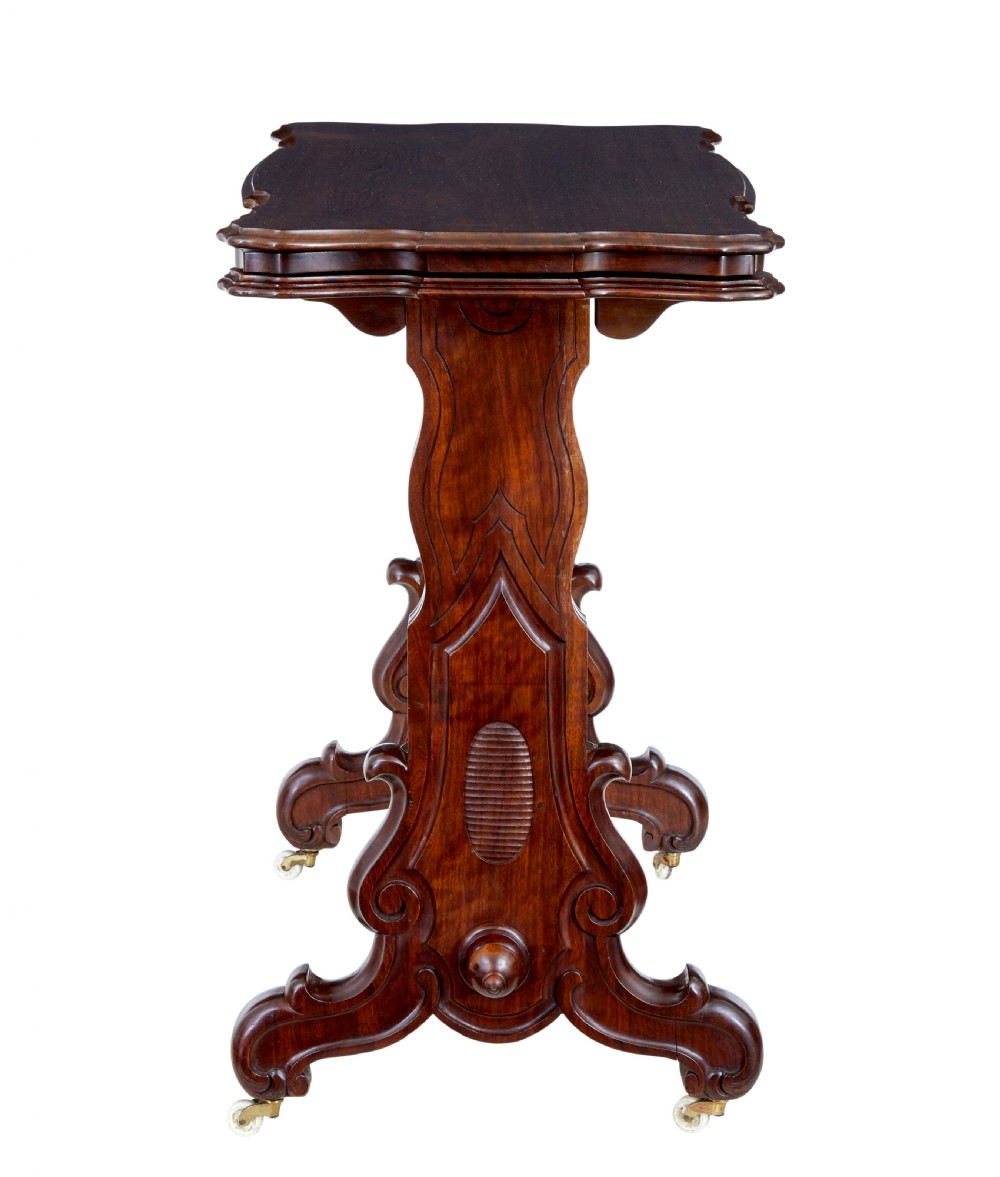 A 19th-century Victorian walnut metamorphic dumb waiter featuring a serpentine moulded top, carved C-scroll side supports, a turned stretcher, and brass castors. View V