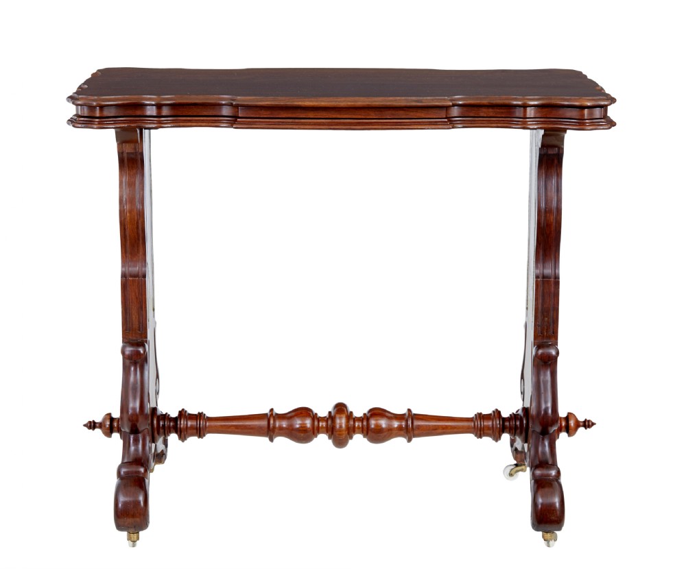A 19th-century Victorian walnut metamorphic dumb waiter featuring a serpentine moulded top, carved C-scroll side supports, a turned stretcher, and brass castors. View VI