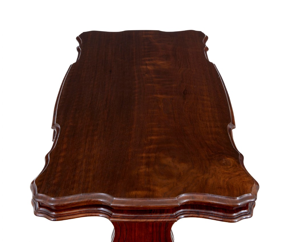 A 19th-century Victorian walnut metamorphic dumb waiter featuring a serpentine moulded top, carved C-scroll side supports, a turned stretcher, and brass castors. View VII
