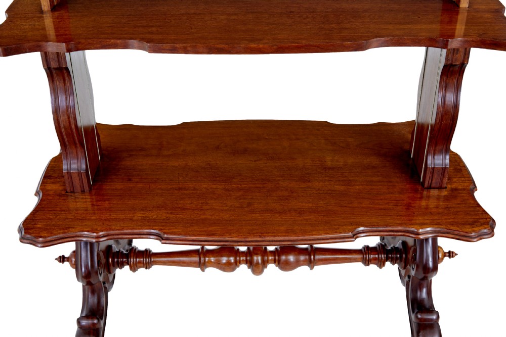 A 19th-century Victorian walnut metamorphic dumb waiter featuring a serpentine moulded top, carved C-scroll side supports, a turned stretcher, and brass castors. View IX