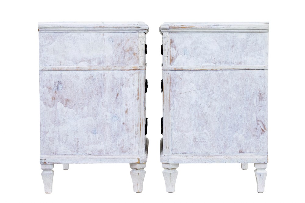 A pair of 19th-century Swedish chests of drawers featuring three drawers each, diamond lattice carvings on the top drawer front, brass handles, and a distressed white paint finish. View V