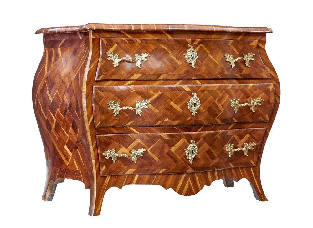 An early 18th-century Rococo bombe chest of drawers featuring geometric parquetry inlay in plumwood and three drawers with ornate brass handles.